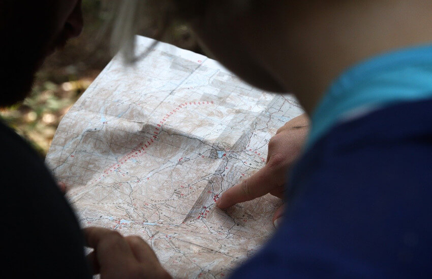 Eine Frau und ein Mann schauen auf eine Landkarte, wobei der Mann einen Punkt mit dem Finger markiert.